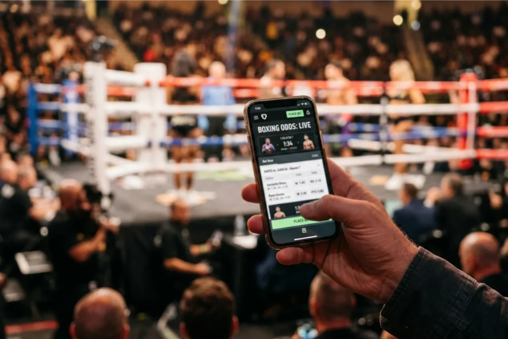 Hand hält Smartphone mit geöffneter Sportwetten-App vor einem Boxring